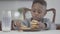 Portrait of cute african american child boy with dirty lips after milk making cookie pyramid sitting by the table in