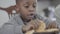 Portrait of cute african american child boy with dirty lips after milk playing with cookies sitting by the table in