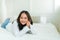Portrait Cute Asian teen with long hair Wearing a white shirt and lazing around in bed happily in the bedroom