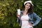 Portrait of cute attractive girl in hat with glass of cold drink with straw in park nature