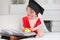 Portrait of cute baby boy in graduation cap holding apple and reading book. Concept of early child education