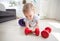 Portrait of cute baby boy palying with red dumbbells on floor at home