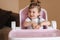 Portrait of cute baby girl sitting in high chair in the kitchen. Adorable little girl waiting for dinner