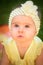 Portrait of cute baby girl in yellow band and dress sits in sunny backyard. 8 months old infant outdoors