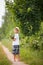 Portrait of cute bare feet kid boy in straw hat standing on a countryside road and holding bunch of wild flowers. Child walking in