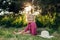 Portrait of cute beautiful blonde Caucasian girl in red pink dress with messy untidy hair sitting on ground grass in park outdoor