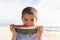 Portrait of cute biracial boy eating large fresh watermelon slice at beach on sunny day