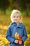 Portrait of a cute blond little boy with maple leaves in autumn park