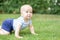 Portrait of cute blond pensive baby boy crawling on green grass lawn outdoors. Thoughtful kid thinking about something. Question o
