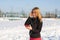 Portrait of a cute blonde girl listening to music while walking down the street holding a red phone in hand. Snow lies around