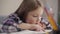 Portrait of cute brunette caucasian girl reading book at the table. Close-up of schoolchild doing homework at home