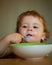 Portrait of cute Caucasian child kid with spoon. Hungry messy baby with plate.