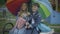 Portrait of cute Caucasian schoolchildren sitting under colorful umbrella on playground and talking. Happy boy and girl