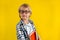 Portrait of cute and clever blonde Caucasian boy in a checked shirt on yellow background. 1 September day. Education and