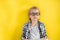 Portrait of cute and clever blonde Caucasian boy in a checked shirt on yellow background. 1 September day. Education and