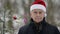 Portrait of cute elderly man with red Santa hat in forest with Christmas tree