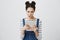 Portrait of cute european girl with trendy two buns hairstyle, wearing overalls and looking excited or interested at