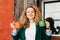 Portrait of cute female with pure skin having stylish hairstyle dressed in green jacket and white T-shirt holding two cups of tea