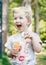 Portrait of cute funny little blond Caucasian child girl toddler standing in the green forest field meadow blowing soap bubbles