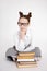 Portrait of cute girl in school uniform and eyeglasses sitting with heap of books over white background