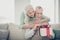 Portrait of cute grandparents dressed sweaters holding package opening looking sitting divan room apartment