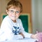 Portrait of cute happy school kid boy with glasses at home making homework. Little child writing with colorful pencils