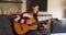 Portrait of cute Latina female lounging at home, playing guitar and singing