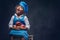 Portrait of a cute little boy with brown curly hair dressed in a blue cook uniform holds apples sitting on a wooden