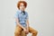 Portrait of cute little boy with curly ginger hair looking in camera with serious expression, sitting on a box, posing