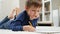 Portrait of cute little boy doing homework on carpet in living room. Concept of domestic education and child development