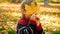 Portrait of cute little boy looking through yellow mapple tree leaf at autumn park