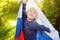 Portrait of cute little boy in public summer park with russian flag on background. Fans child supporting and cheering their