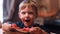 Portrait of cute little boy sitting at table. Boy making funny face and talking, holding piece and eating watermelon.