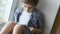 PORTRAIT: Cute little boy uses a white tablet PC on a windowsill at home