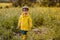 Portrait of cute little boy in yellow raincoat, rubber boots and cap holding wooden stick