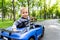 Portrait of cute little caucasain blond toddler boy enjoy having fun riding electric powered toy car by asphalt path