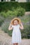 Portrait of a cute little curly blue-eyed girl 3 years old in a wicker hat and white sundress near blooming lavender. happy child