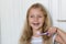 Portrait of cute little girl with blonde hair which cleaning tooth with brush and toothpaste in bathroom