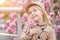 Portrait of cute little girl with blonde hair which holding hand pink flower of magnolia. Spring season