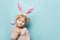 Portrait of a cute little girl dressed in Easter bunny ears holding colorful egg on blue background