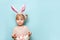 Portrait of a cute little girl dressed in Easter bunny ears holding colorful egg on blue background