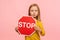 Portrait of cute little girl holding Stop symbol, red traffic sign and looking with serious responsible expression