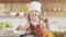 Portrait of a cute little girl in the kitchen dressed as a professional cook looking into the camera and smiling. She