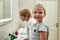 Portrait of cute little girl looking at camera while washing her face, brushing teeth together with her sibling brother