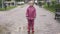 Portrait of cute little girl in pink waterproof costume and rubber boots standing in puddle and looking at camera