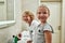 Portrait of cute little girl smiling at camera while washing her face, brushing teeth together with her sibling brother