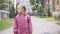 Portrait of cute little girl in waterproof coat walking along the alley outdoors. Pretty Caucasian child in pink clothes