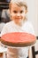 Portrait of a cute little happy candid caucasian five year old kid boy in white t-shirt holds a homemade baked cake or pie in his