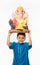 Portrait of cute little Indian boy holding a Ganesh idol or lord ganesha or ganapati murti /statue over his head, taking home on G