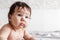 Portrait of cute naked baby lying on bed blanket at home, blurred white background. Infant child crawl on tummy in